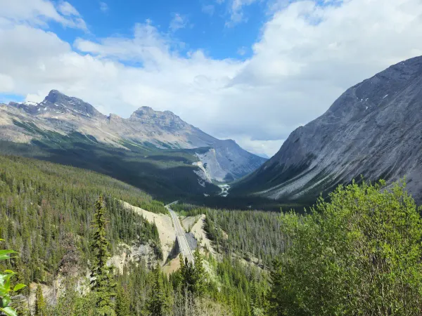 Aerial view of the Icefields Parkway road winding through a forested valley with mountains rising on both sides, Banff National Park, Canada