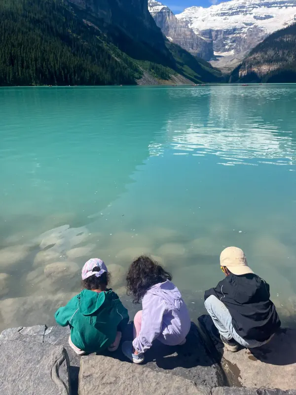 Three children backs to camera in colourful rain coats looking at Lake Louise Banff National Park Canadian Rockies
