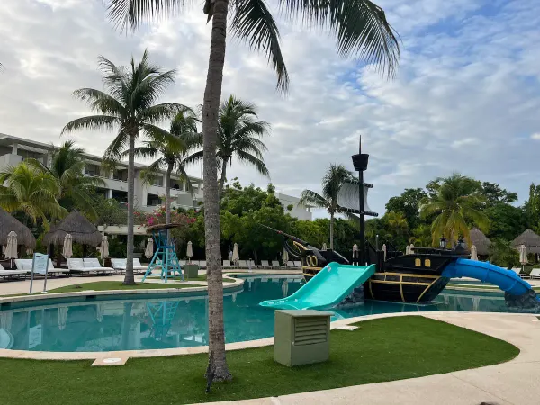 Pirate ship-themed pool with slides at Paradisus Playa del Carmen La Esmeralda, empty in the early morning light, palm trees surrounding.