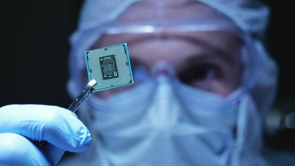 in Ultra Modern Electronic Manufacturing Factory Design Engineer in Sterile Coverall Holds Microchip with symbols in futuristic holography.