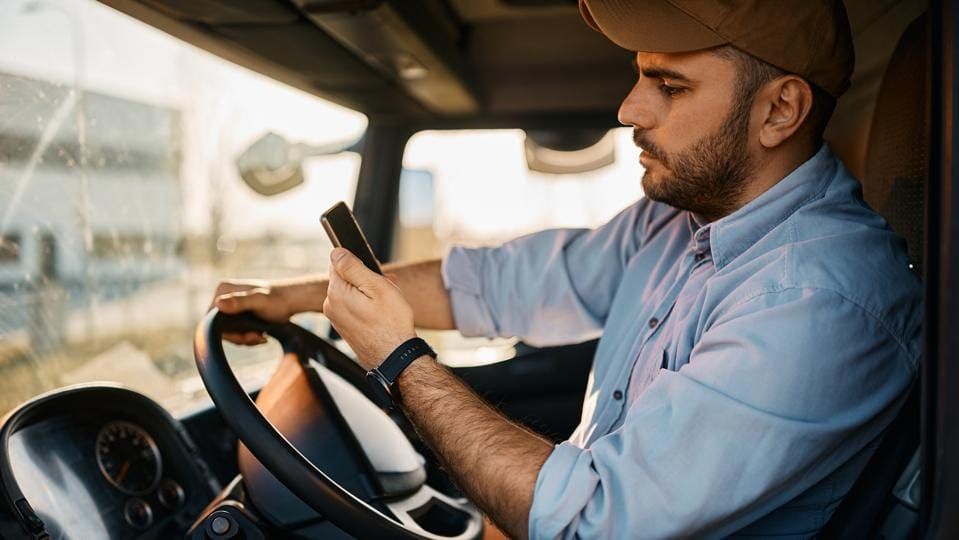 Side view of truck driver reading text message on smart phone while driving.