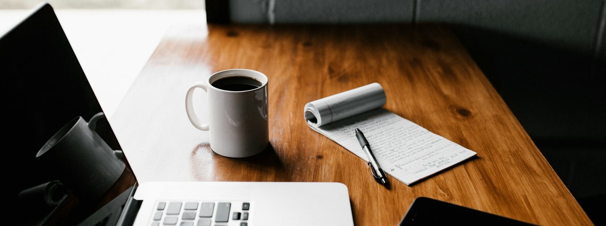 MacBook Pro, white ceramic mug,and black smartphone on table