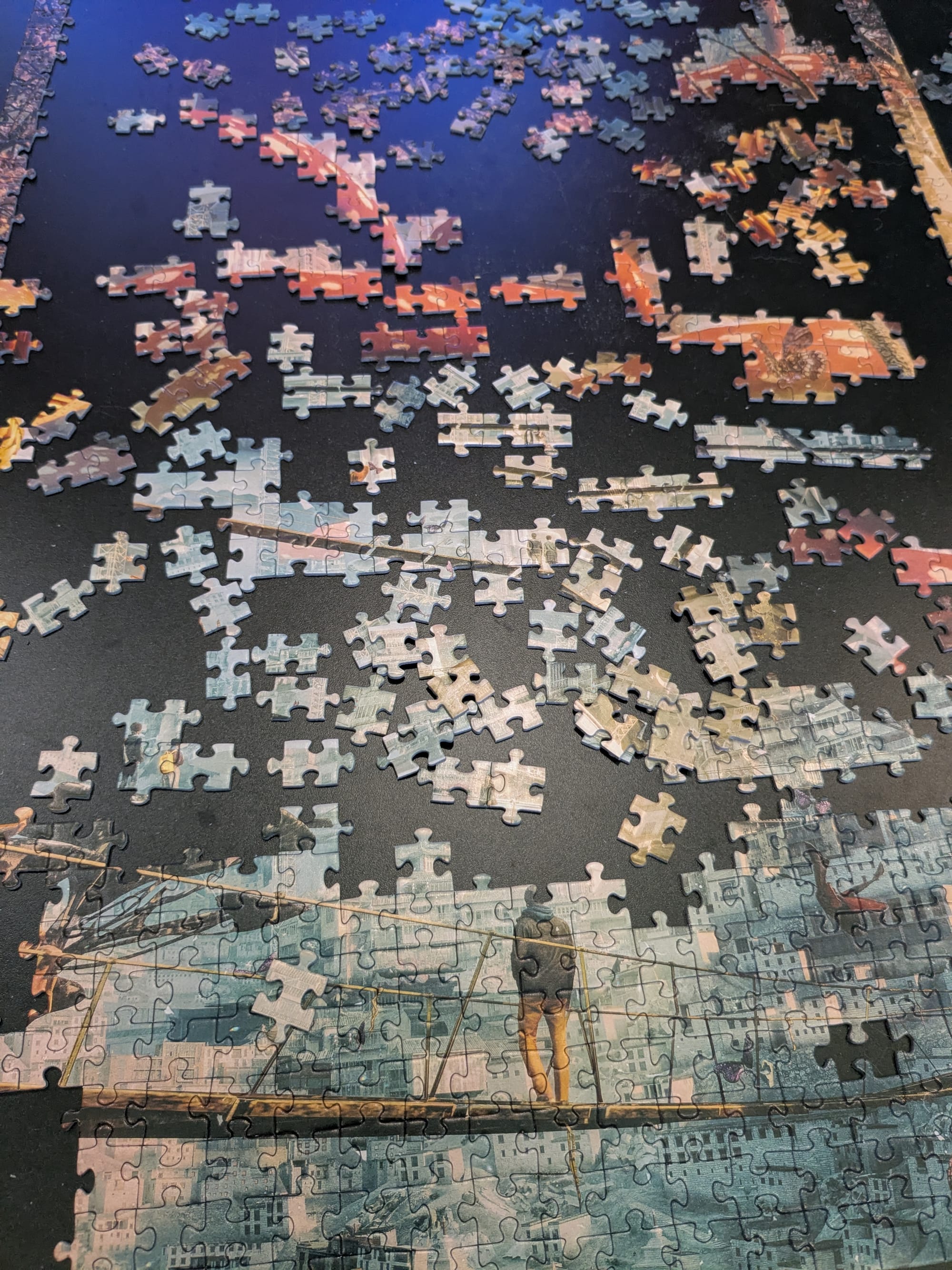A half finished puzzle on a black coffee table, that depicts a person on a bridge looking out over a large city