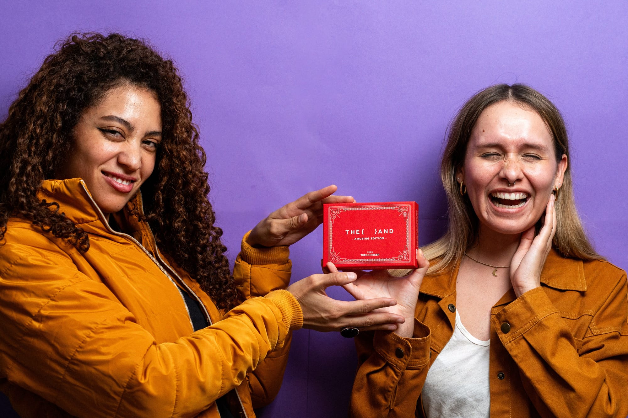 Picture of two female friends laughing holding {THE AND} Amusing card game for couples, friends and family