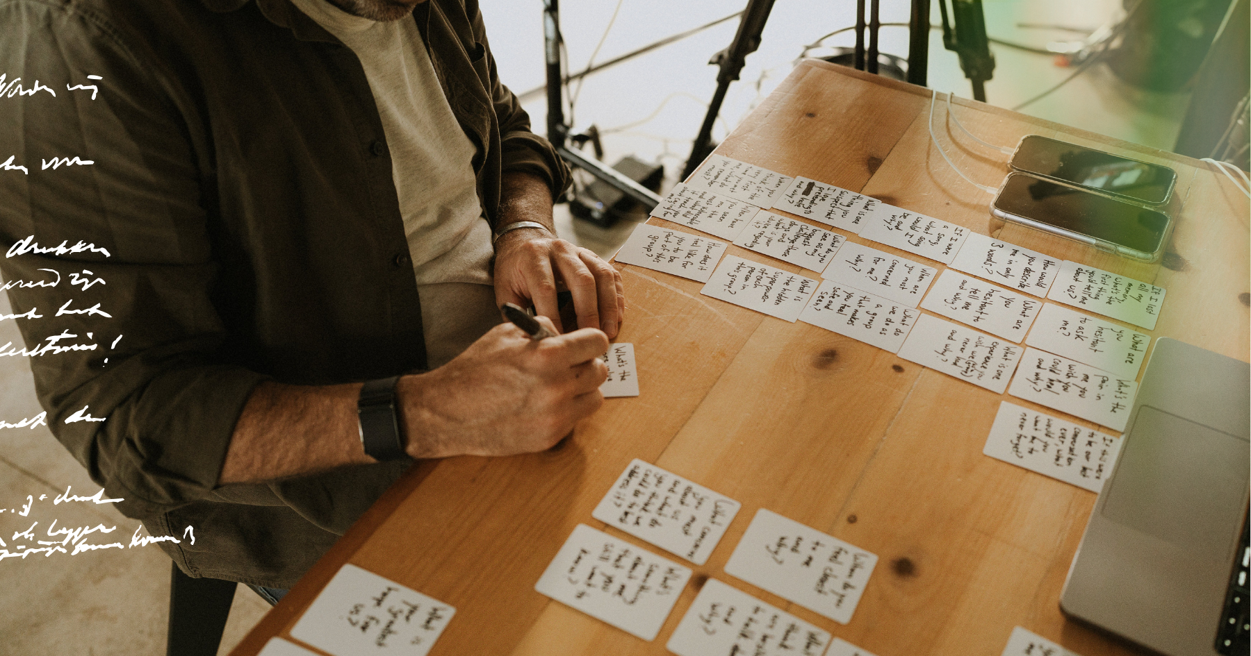 Picture of question cards on a wooden table and a man writing on them