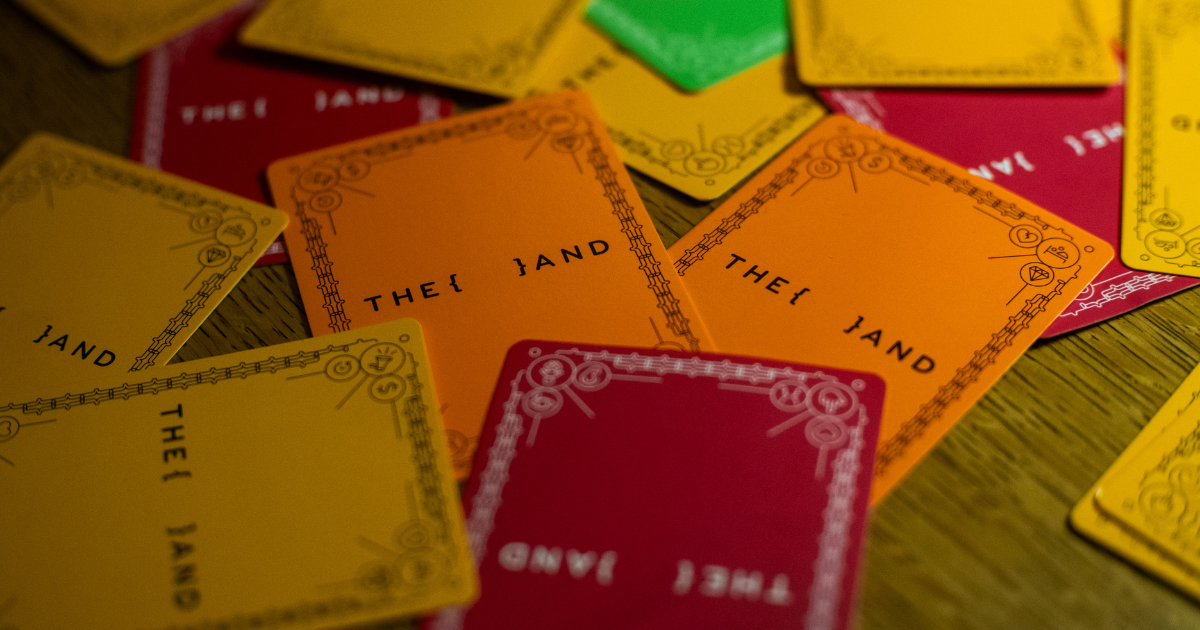 Colorful {THE AND} card game cards spread across a table in orange, yellow, red, and green, displaying the brand's signature design