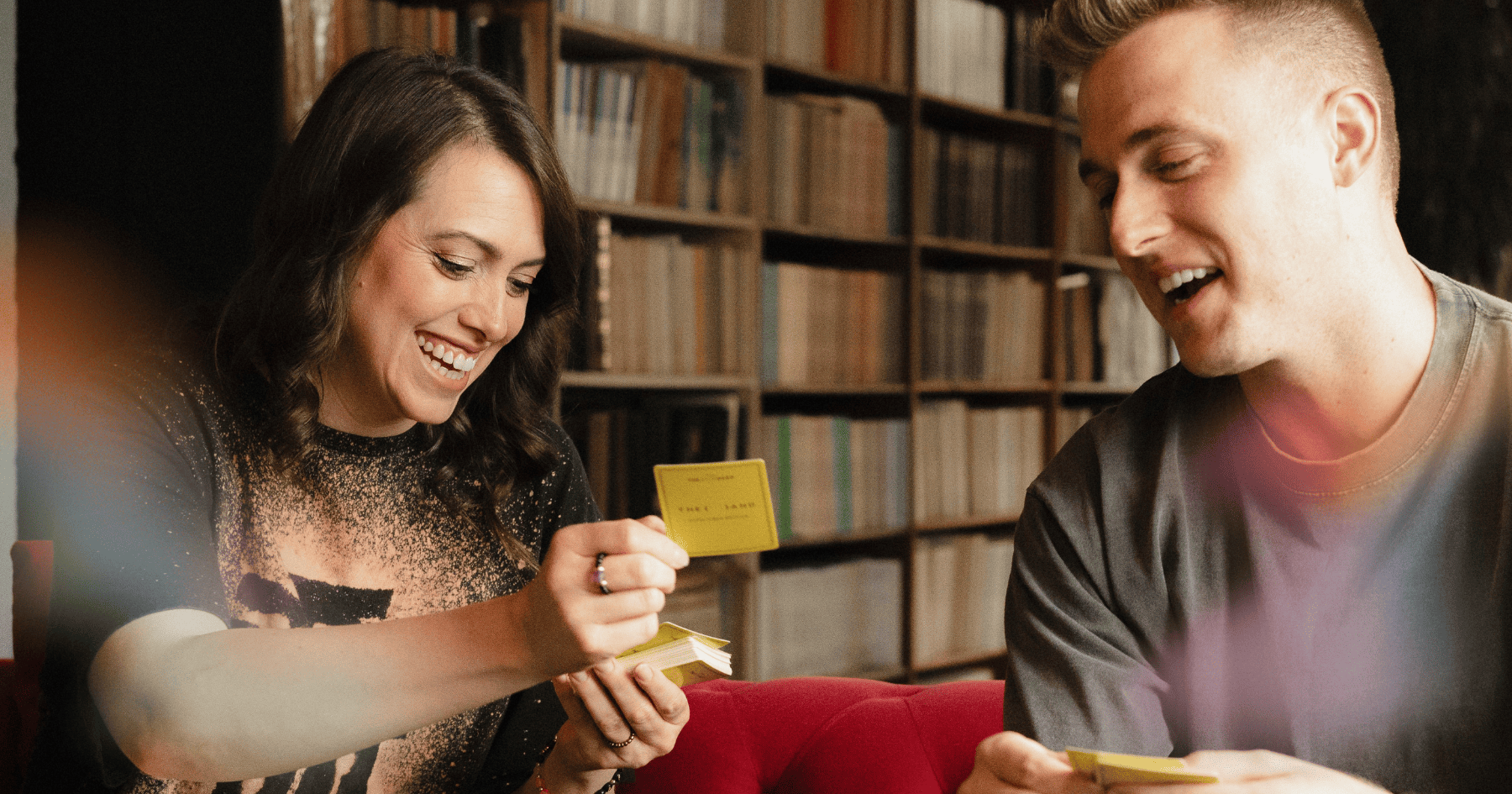 A man and woman from Sunny & The Black Pack playing {THE AND}&nbsp;Good Vibes card game sitting on a couch and laughing