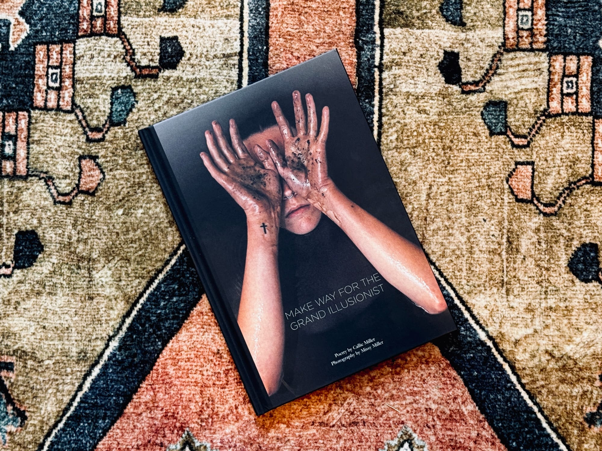 Book cover of "Make Way for the Grand Illusionist" resting on a patterned rug, featuring photography by Missy Miller and poetry by Callie Miller.