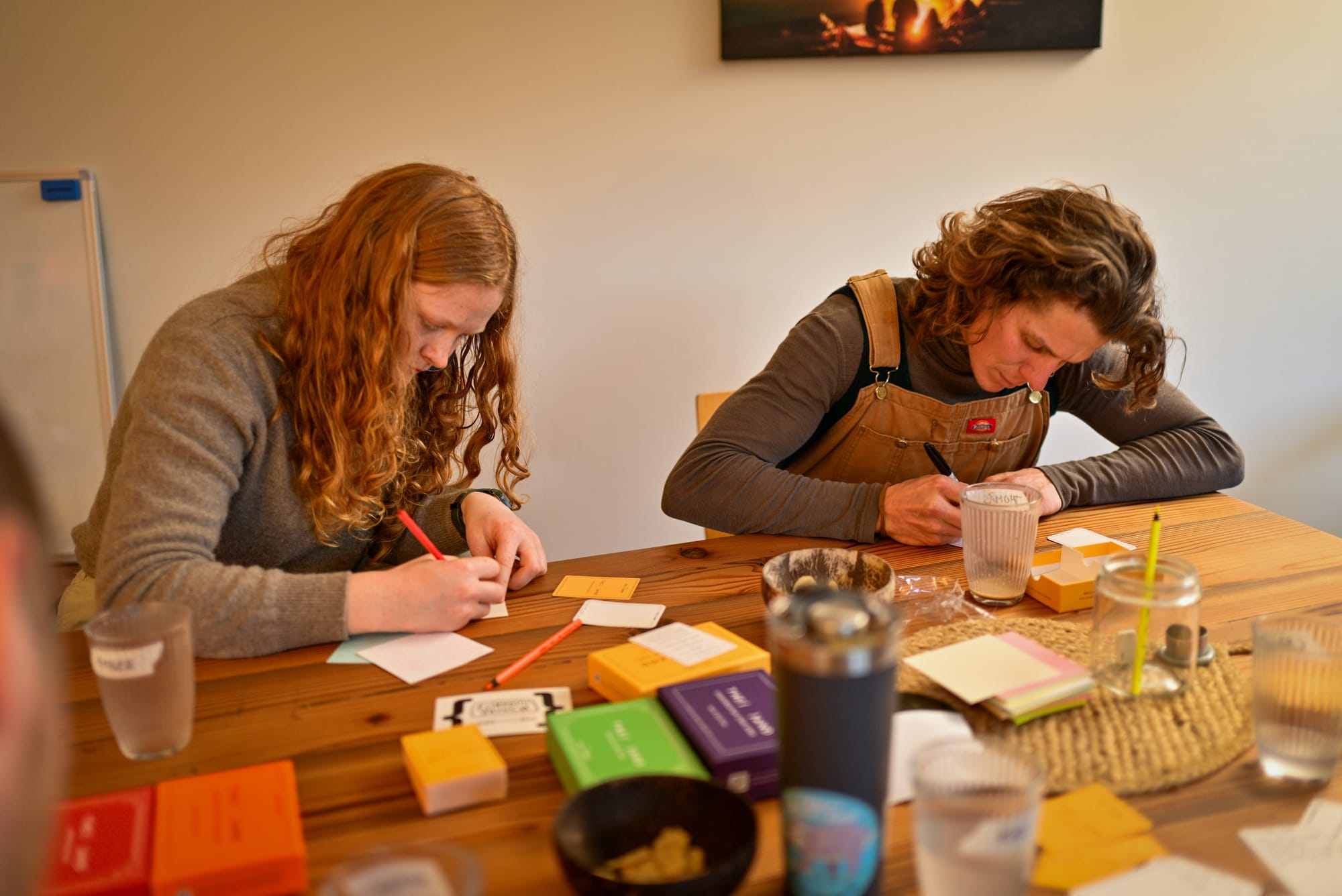 Two guests at Kai's Ōtautahi Christchurch gathering writing on blank cards at a wooden table surrounded by {THE AND} deck boxes.