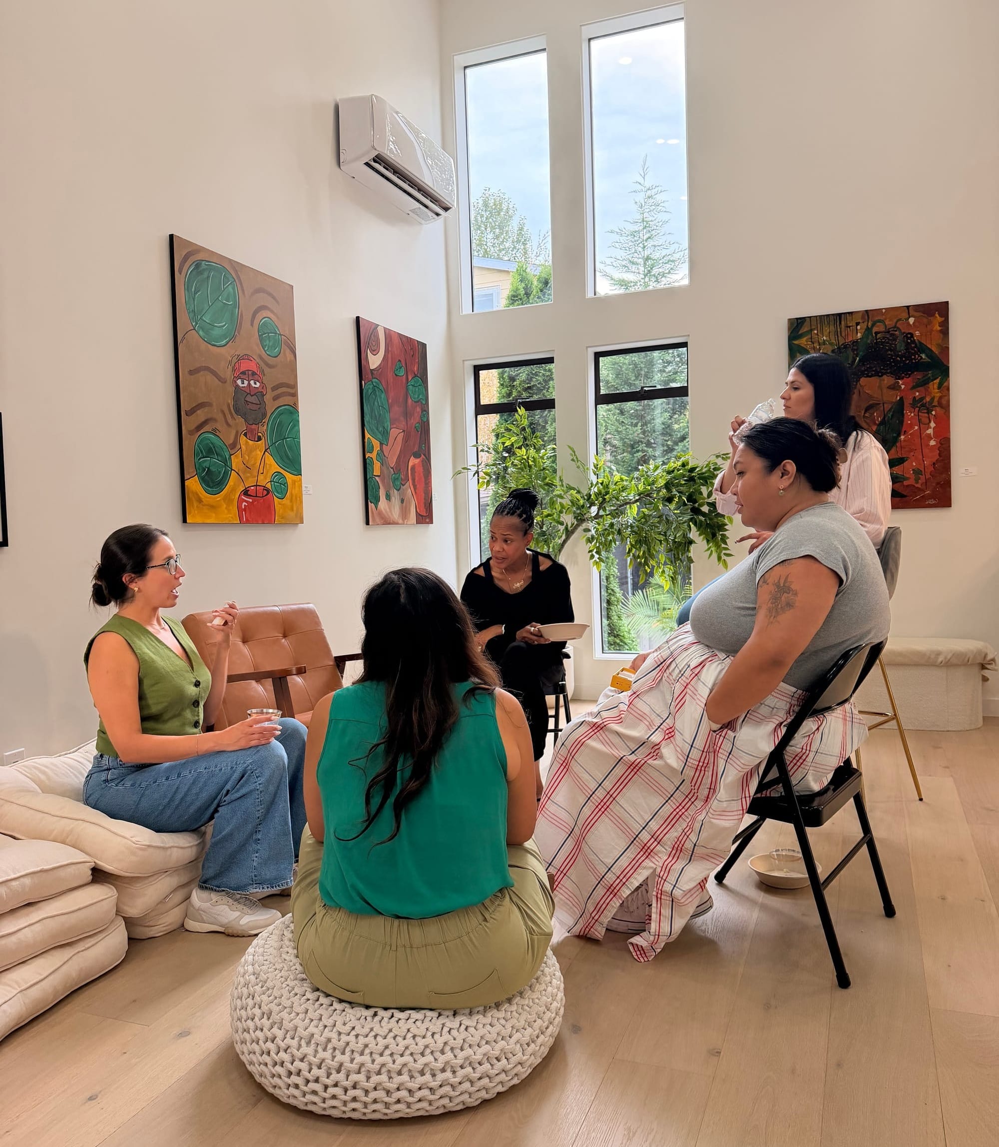 A small circle of women seated together in a bright, art-filled living room at Jennica's Seattle gathering, deep in conversation.