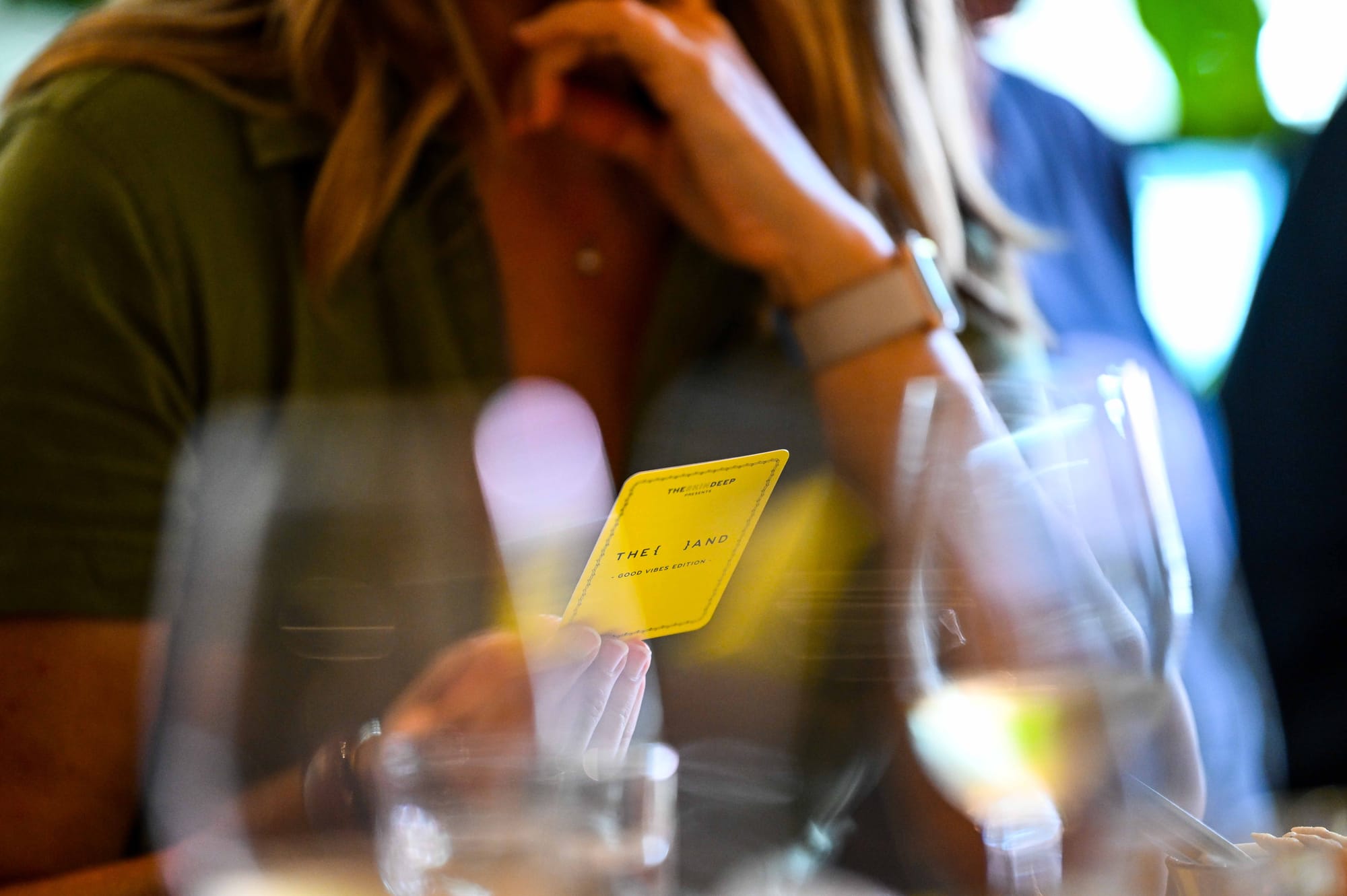 Close-up of a hand holding {THE AND} Good Vibes edition card at Lenna's VinoTeca gathering in Atlanta.