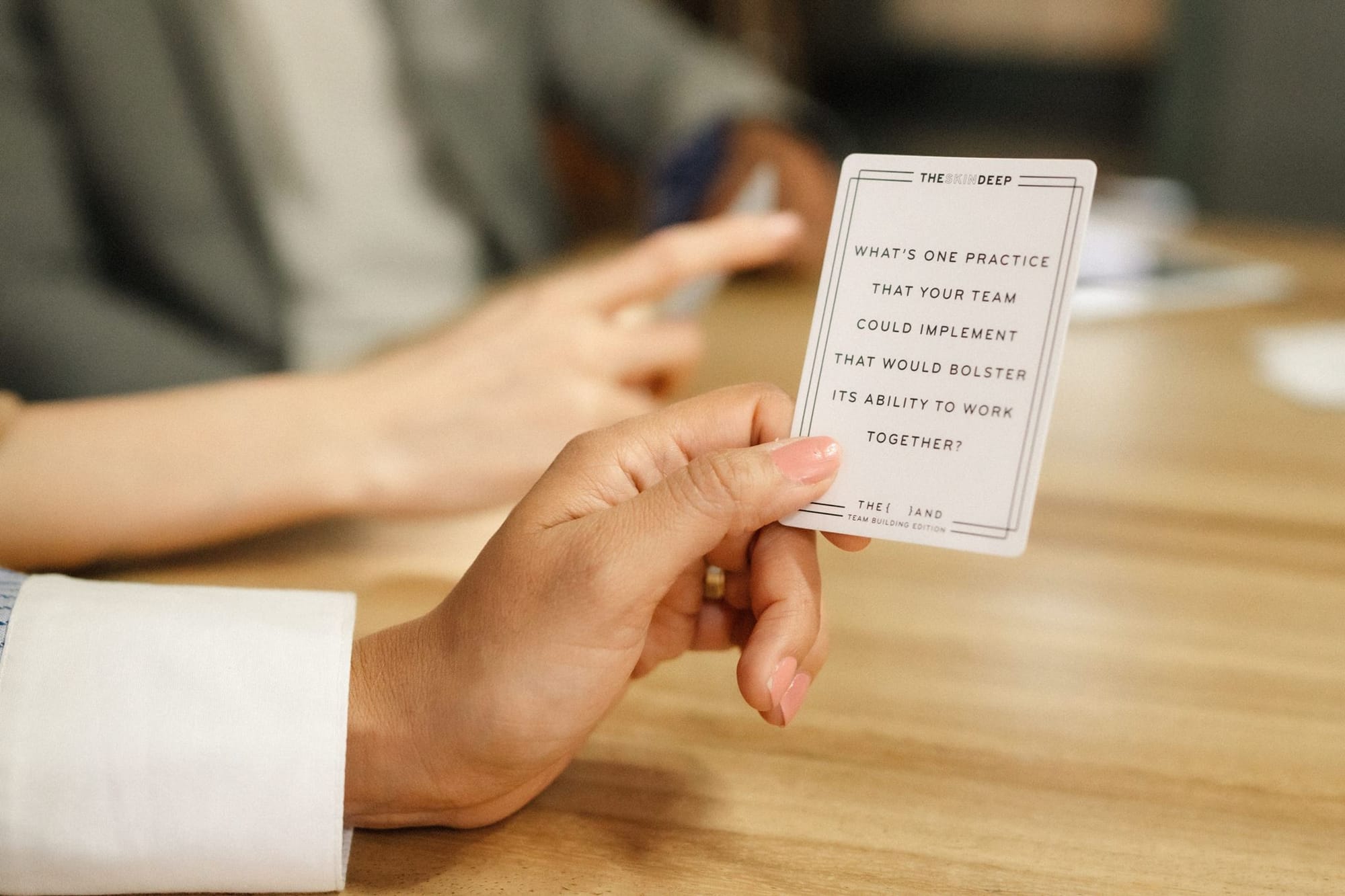 Hand holding a {THE AND} Team Building Edition card that asks which practice could help a team work together.
