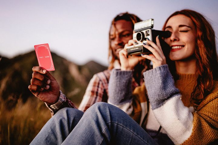 A man and woman playing a dating card game at a picnic with a polaroid camera