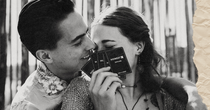 Picture of a couple smiling and whispering while holding cards from the Honest X intimacy card game