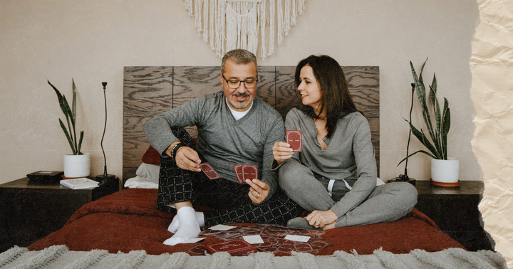 Picture of a couple sitting in bed and playing a card game wearing their pijamas