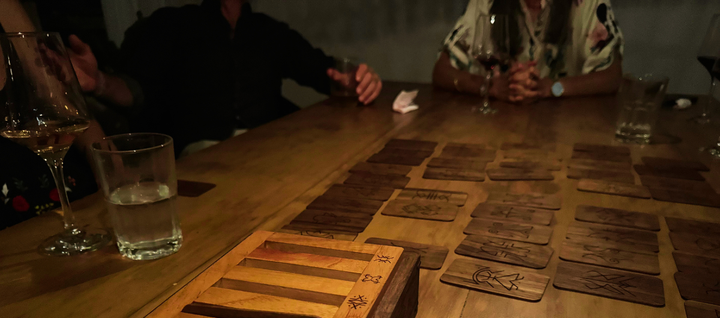 People seated around a dinner table playing a wooden card game called RITUAL