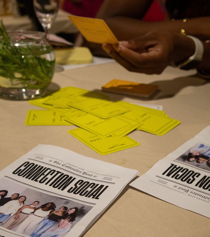 Close-up of a table at Elizabeth's Orlando event with yellow {THE AND} cards spread out, a "Connection Social" printed program, and a guest holding a card.