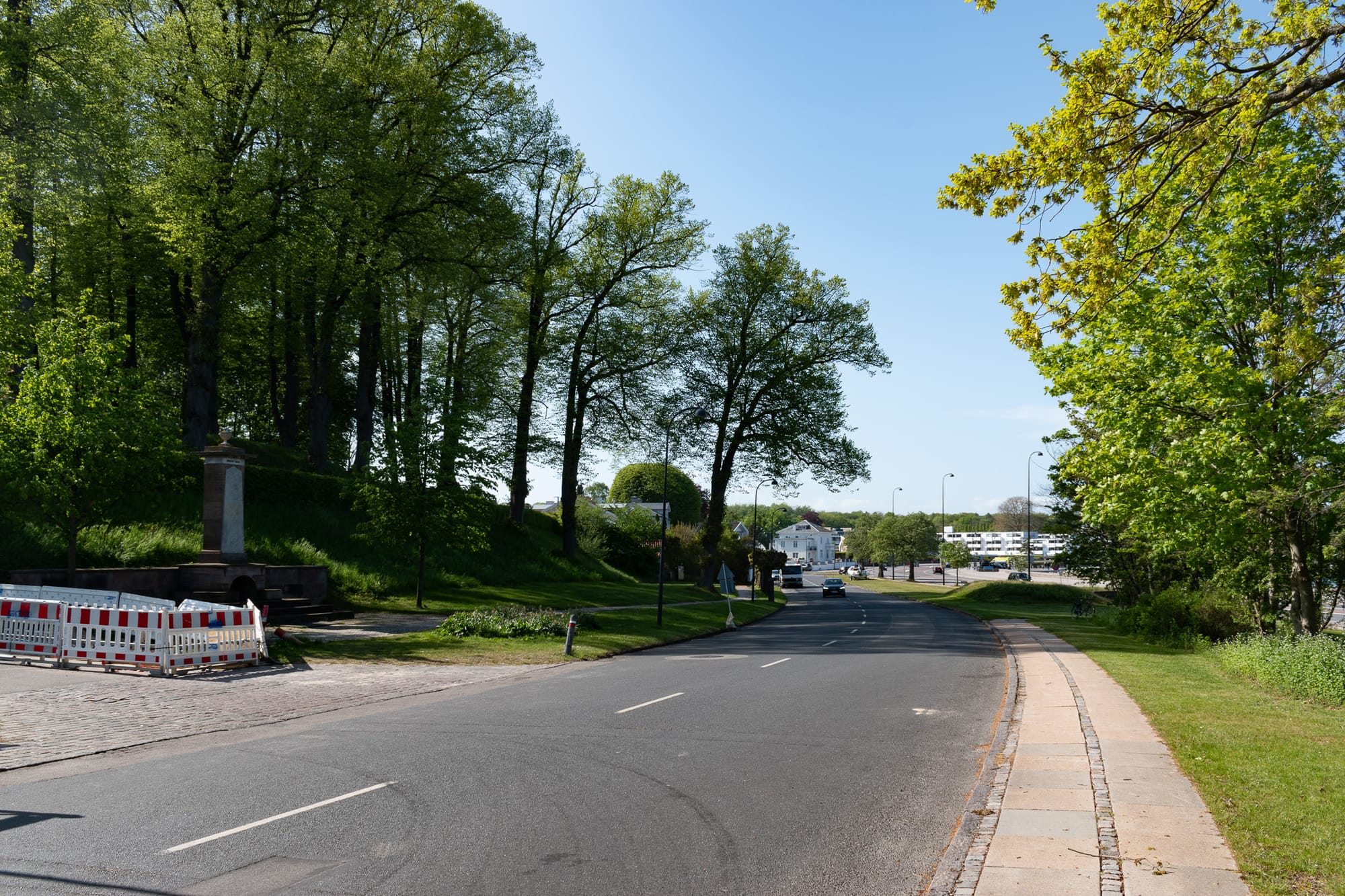 Emiliekilde on the left of the road, a car approaching, trees, white homes in the distance.