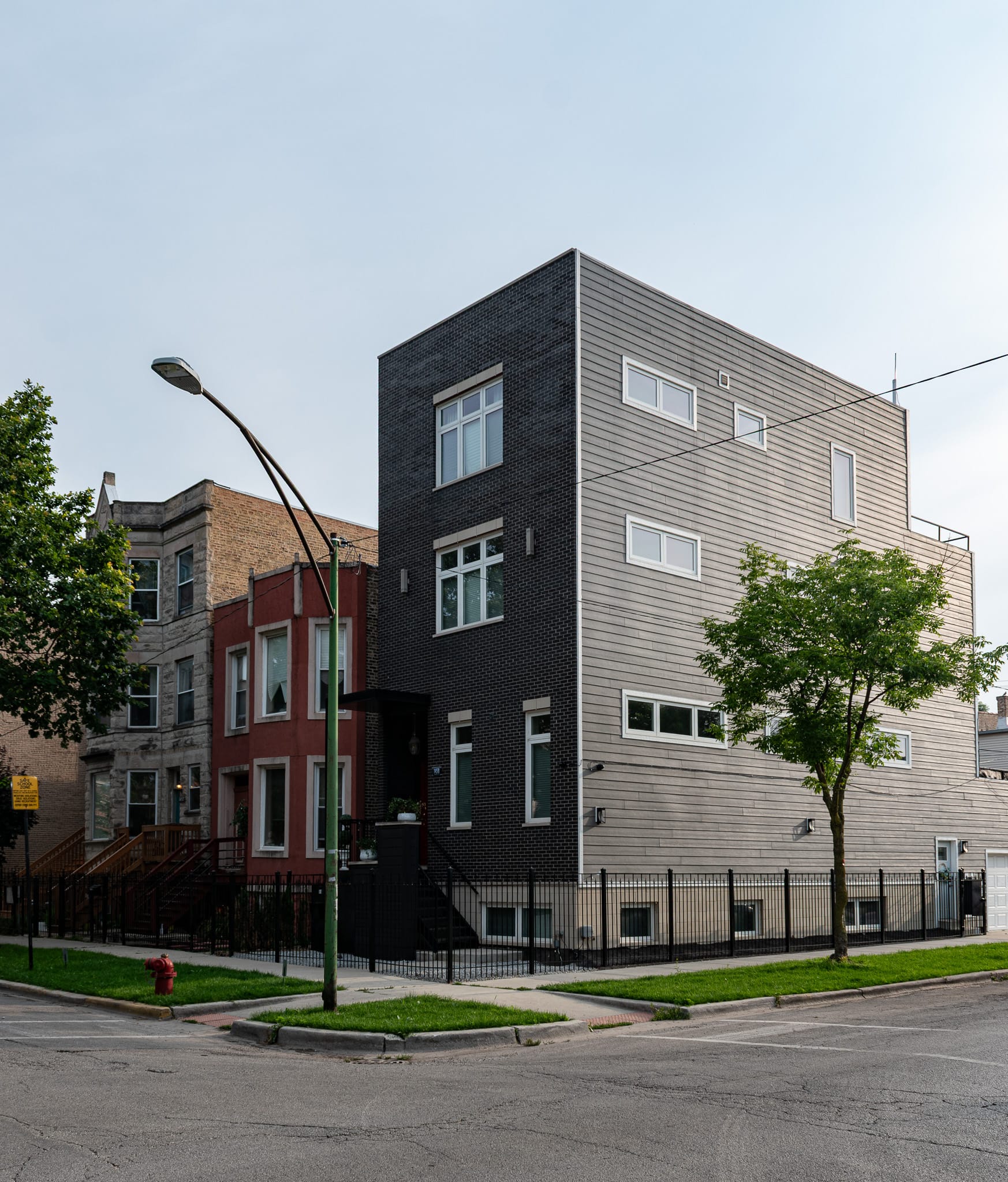A new built three-story building on the corner next to a brick two story building next to a three story greystone