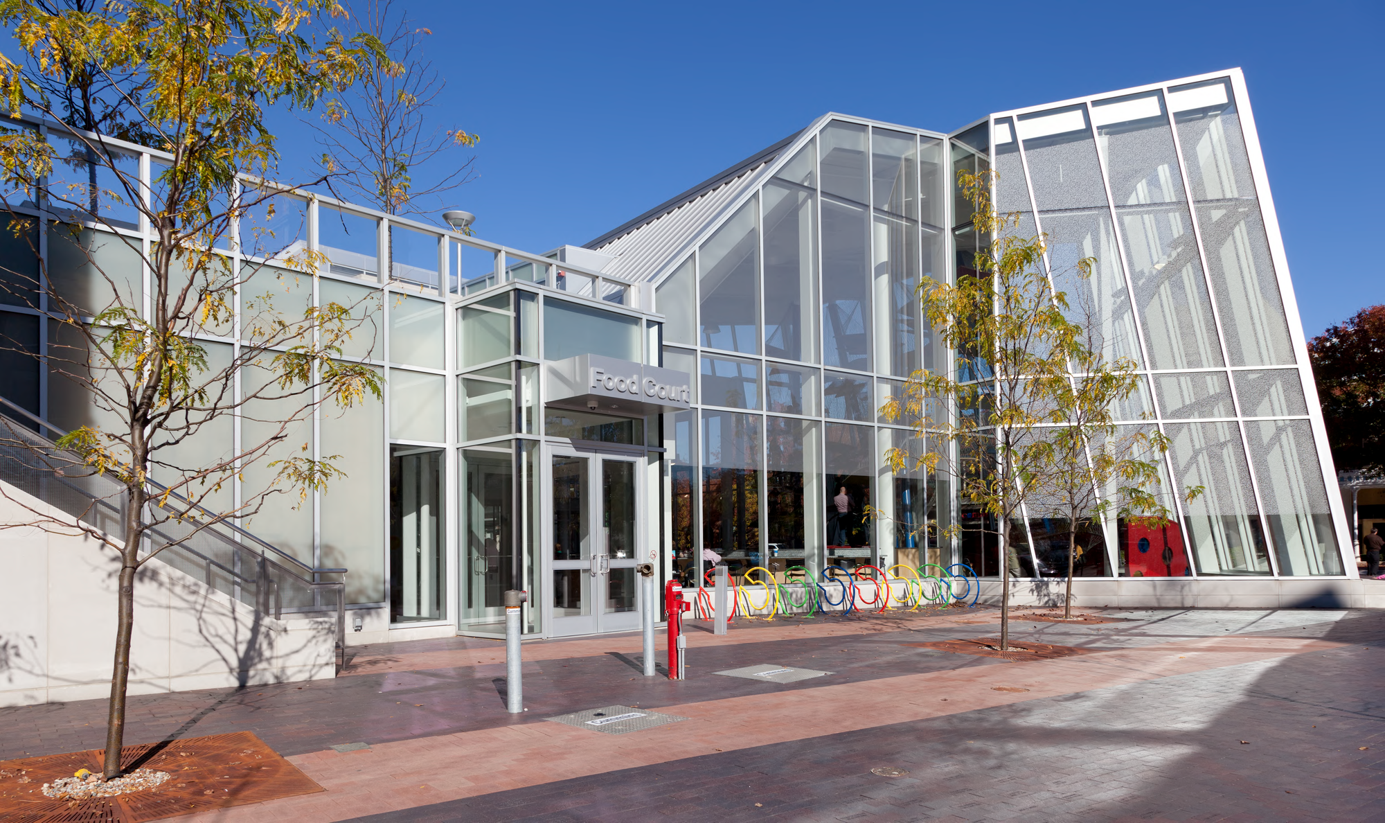 White steel and glass building with a sloping facade and C-shaped bike racks