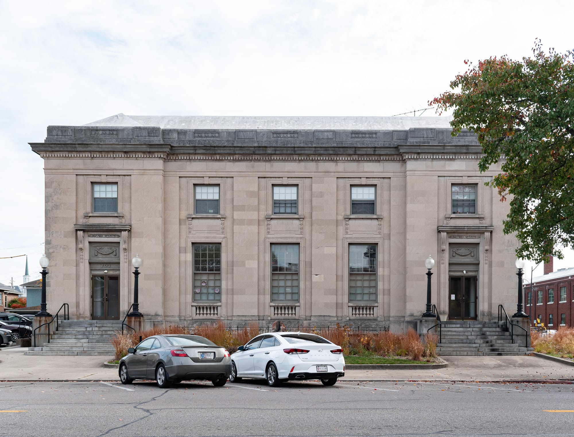 Head-on shot of the limestone-clad, two-story post office, there are two parked cards in front, two main entrances with big staircases