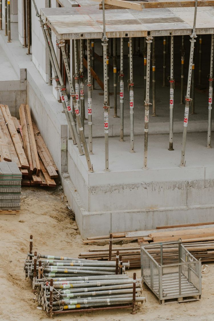 A construction site with concrete foundations and numerous metal scaffolding poles supporting a platform, symbolizing the underlying infrastructure and complexity of data systems.