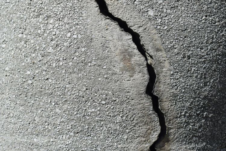 A close-up of a fractured concrete wall with a prominent crack running through weathered grey stone, representing the structural failure that occurs when data pipelines lack clear ownership.