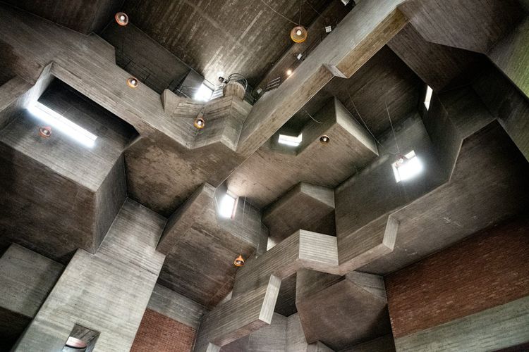 Angular concrete forms and dramatic lighting inside a brutalist structure, representing the deliberate design of spaces where different roles can collaborate and build toward a common goal.