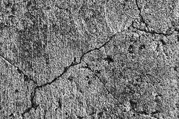 A black and white close-up of a cracked concrete surface with fracture lines across the frame, representing the silent structural failure that schema drift introduces at the data layer.