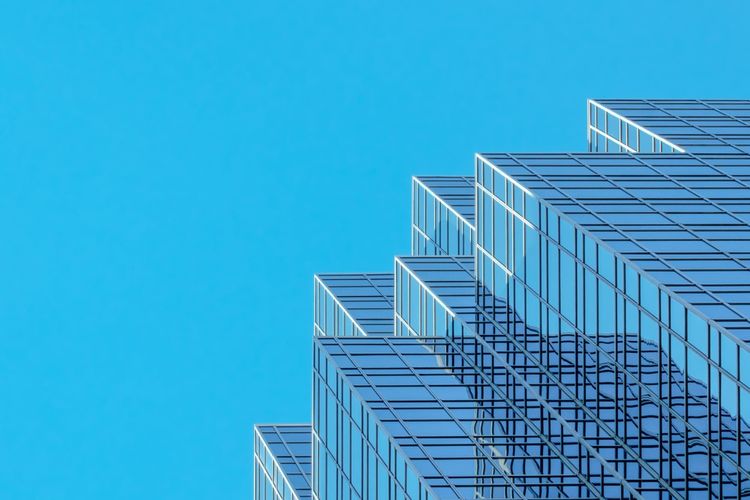 A white and blue glass skyscraper seen from below, floors stacked against a clear blue sky, representing the layered data infrastructure that AI workloads inherit from beneath.