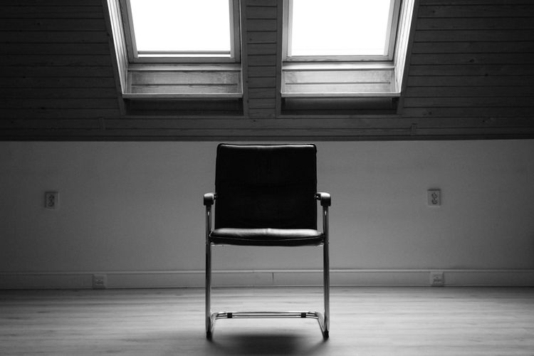 A grayscale photograph of a solitary chair beside a window, its seat empty in a quiet interior, representing the vacant accountability role that sits between data delivery and business trust.