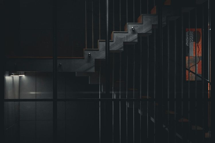 A dark interior staircase with vertical metal railings ascending into shadow, representing a career path that has no defined top for the data engineer climbing it.