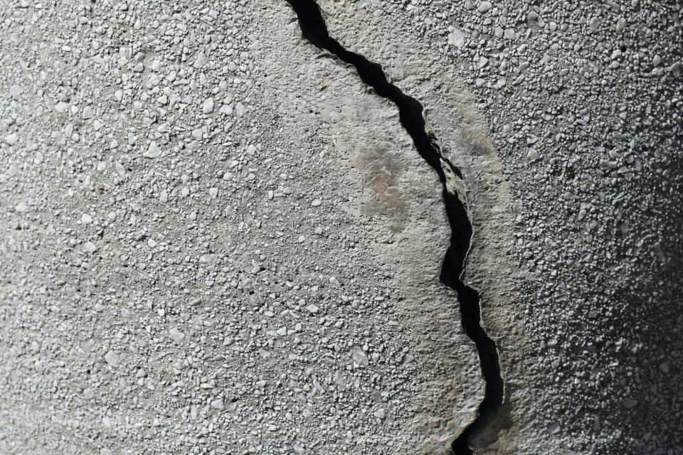 A close-up of a fractured concrete wall with a prominent crack running through weathered grey stone, representing the structural failure that occurs when data pipelines lack clear ownership.