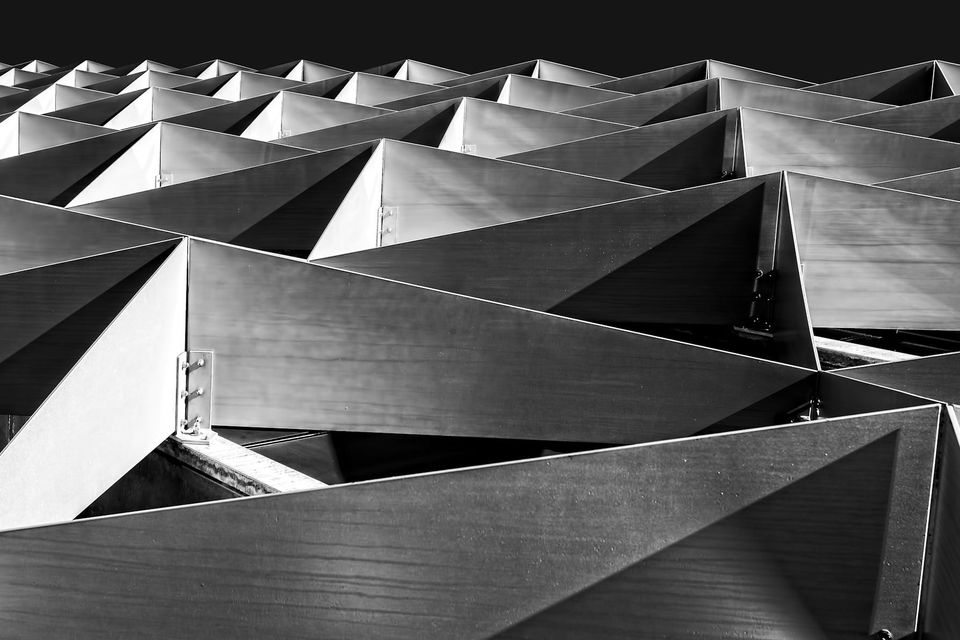 A grayscale close-up of interlocking steel building frames casting angular shadows, representing the structural sequencing that a data platform migration depends on.