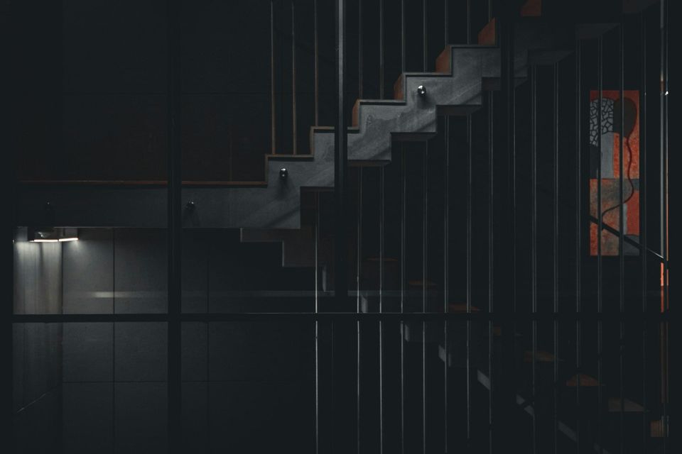 A dark interior staircase with vertical metal railings ascending into shadow, representing a career path that has no defined top for the data engineer climbing it.