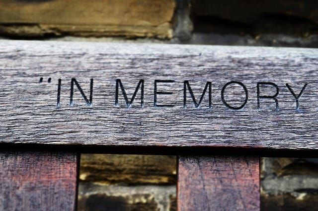 Closeup of wooden bench with the words in memory engraved on the backrest