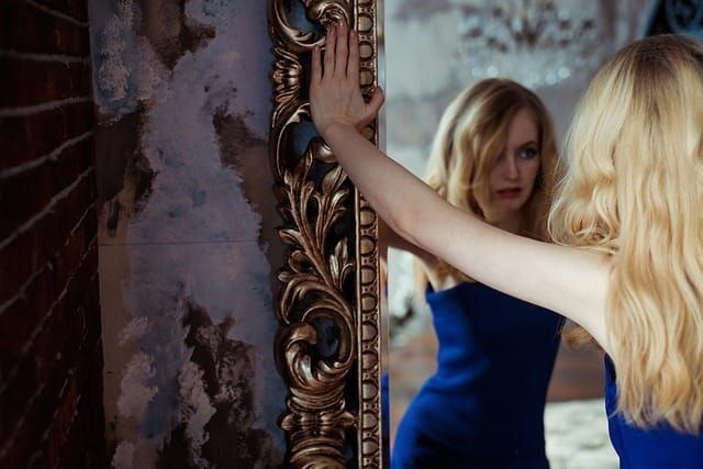 Pretty young blonde woman staring in a mirror with an ornate golden frame