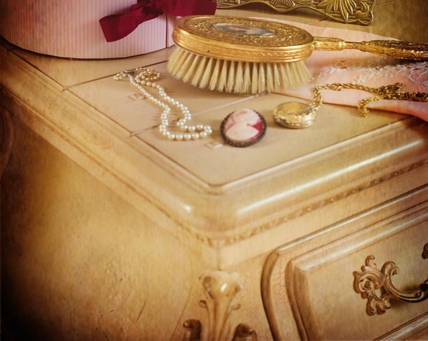 Vintage jewelry and a hairbrush atop an antique white dresser 