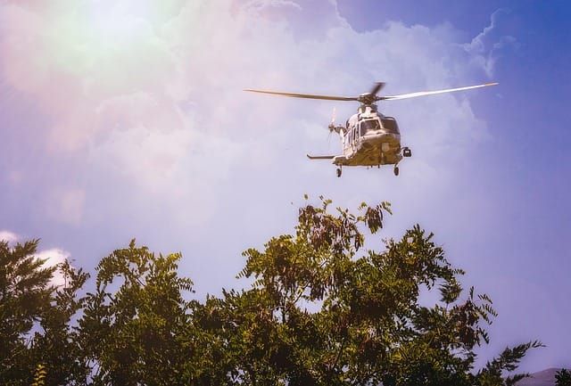 Helicopter in sky above tree with clouds and sun in background