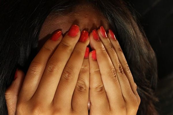 Photo of white woman’s hands with red painted fingernails covering her face in shame 