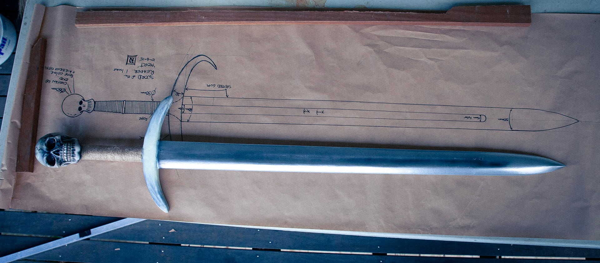 comparing the finished sword to the original design plans 