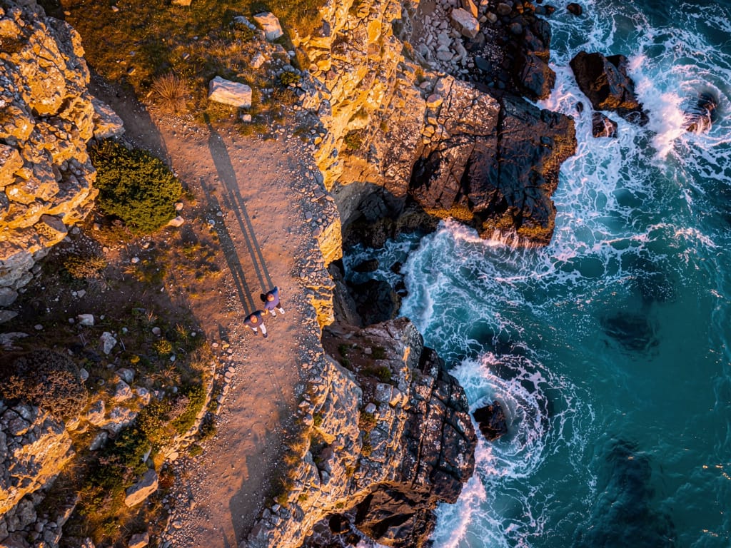 Two men walking and talking on a coastal path.