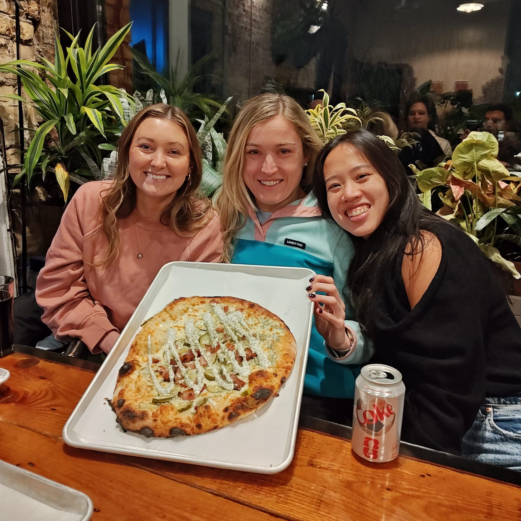 three women holding a dill pickle pizza
