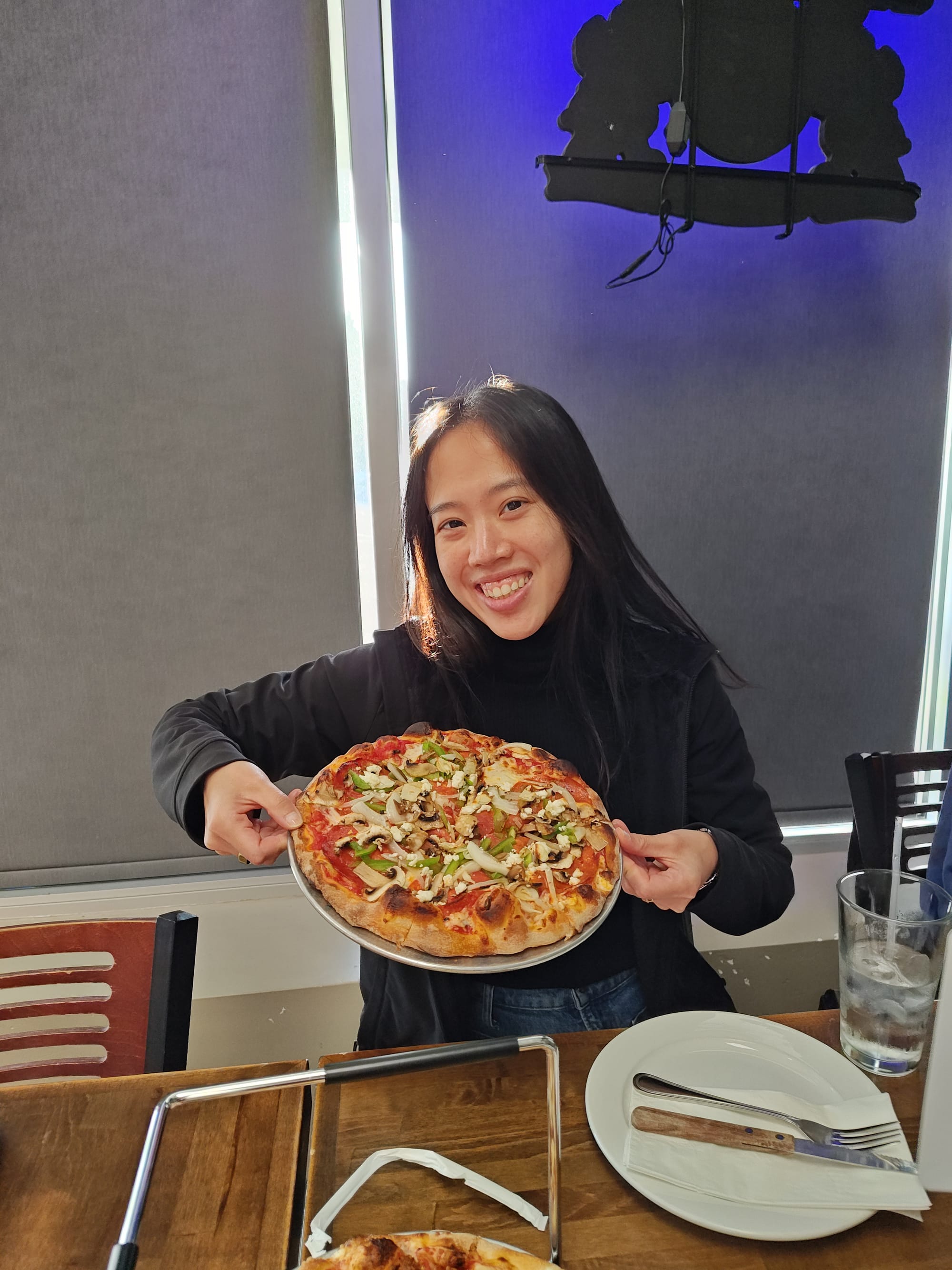 smiling woman holding a pepperoni with feta pizza