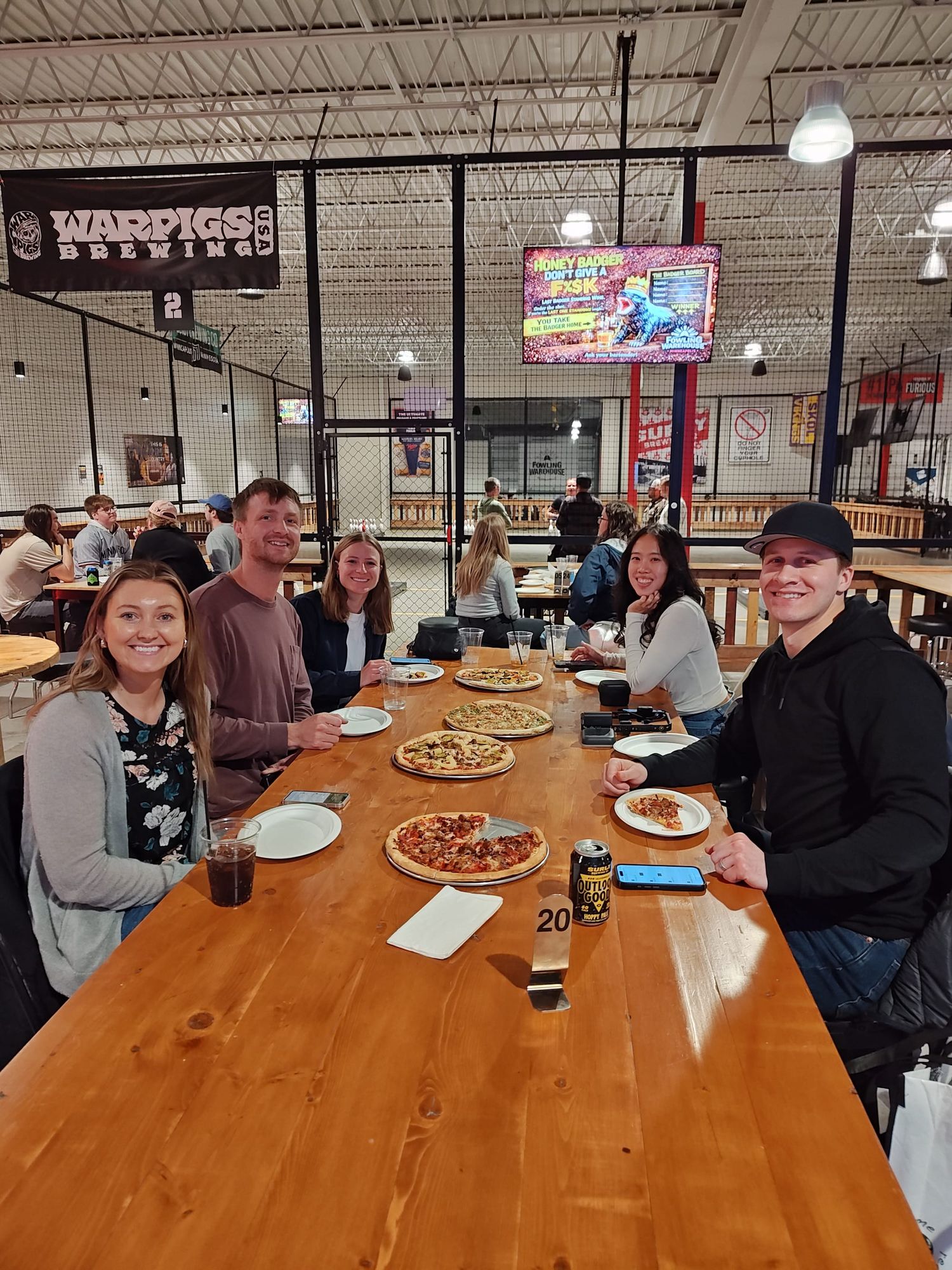 five people smiling and sitting at a table with pizzas on the table