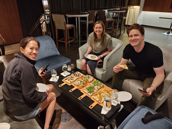 three people smiling and around a table of four pizzas