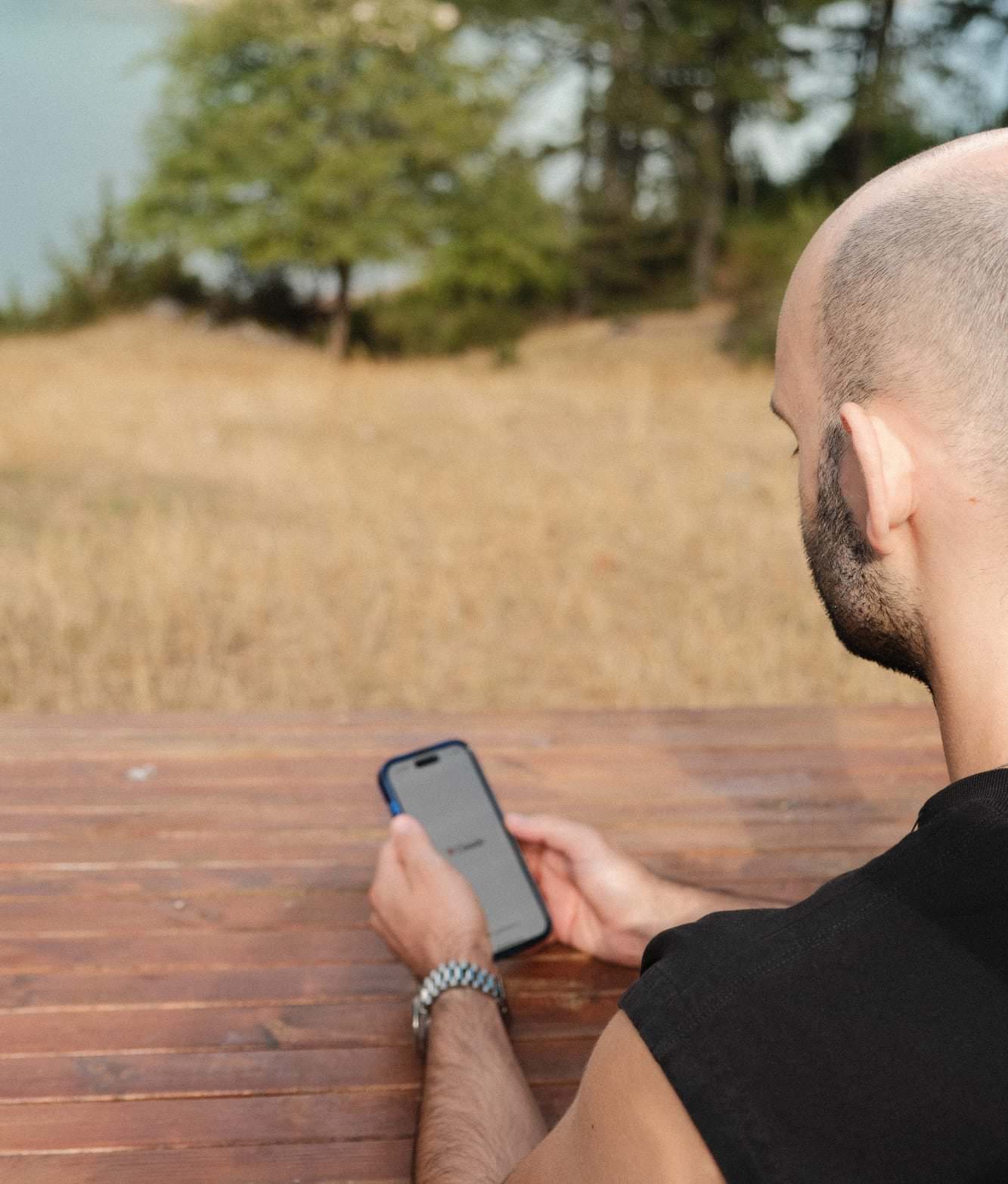 Mann nutzt am Holztisch im Freien sein Smartphone, Sinnbild für die stille, private Nutzung von KI im Alltag