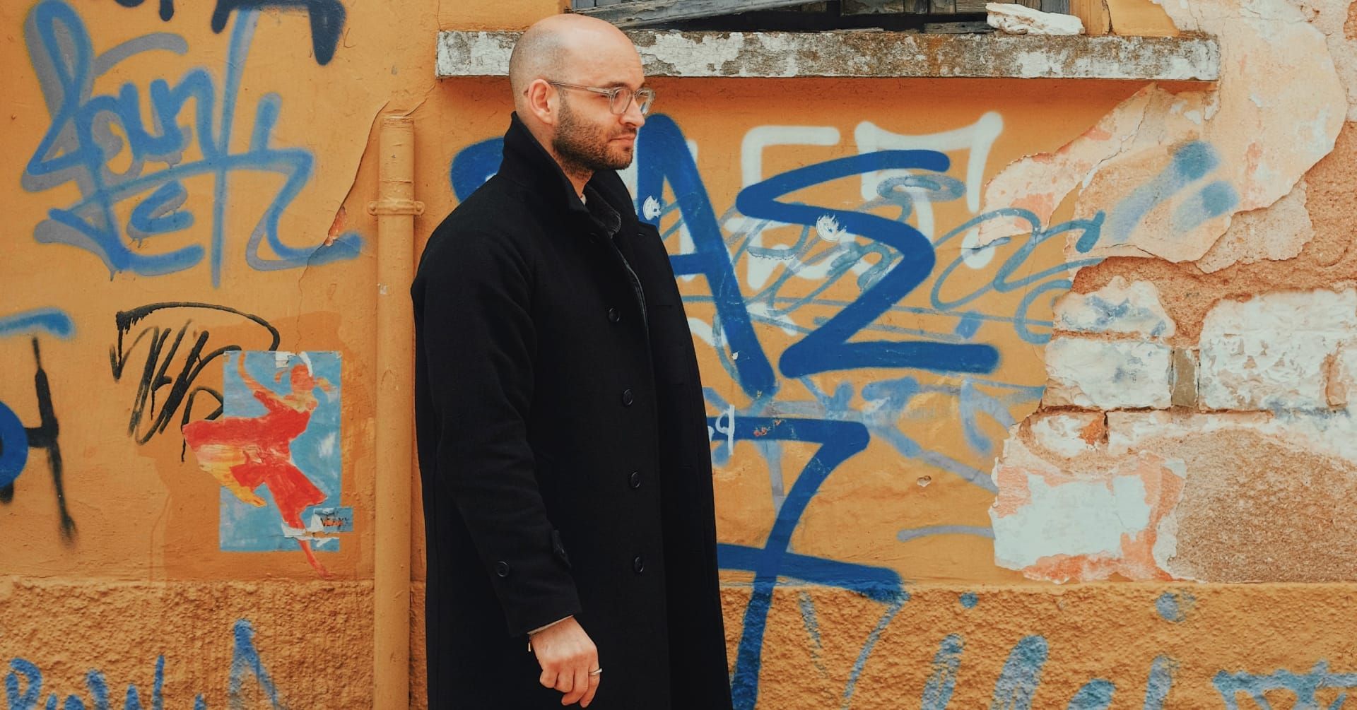 Christos Stavrou vor bemalter Wand mit blauer Graffiti – Episode 13 über Perfektionismus, Authentizität, Echtheit und unperfektes Unternehmertum.