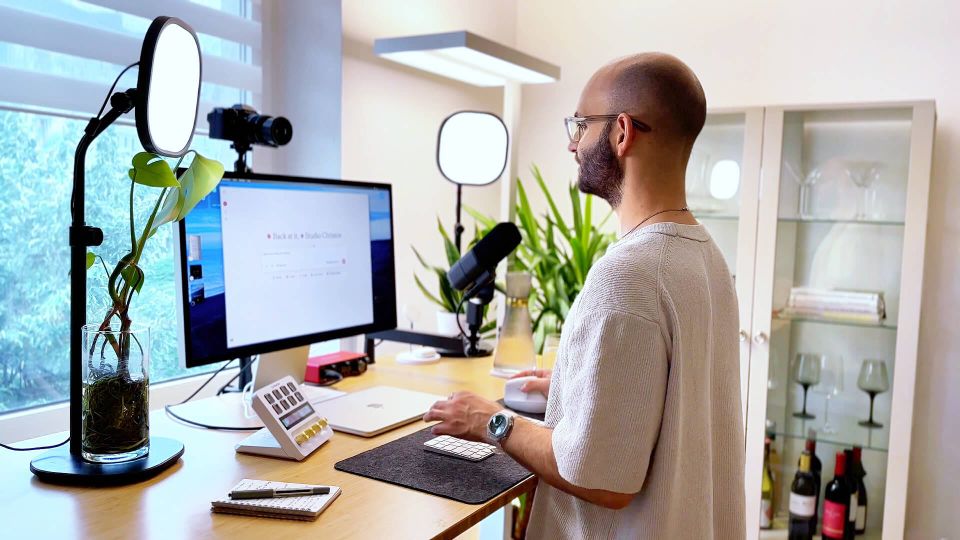 Studio Christos Stavrou arbeitet an seinem ergonomischen Steharbeitsplatz mit Monitor, Podcast-Equipment und Pflanzen