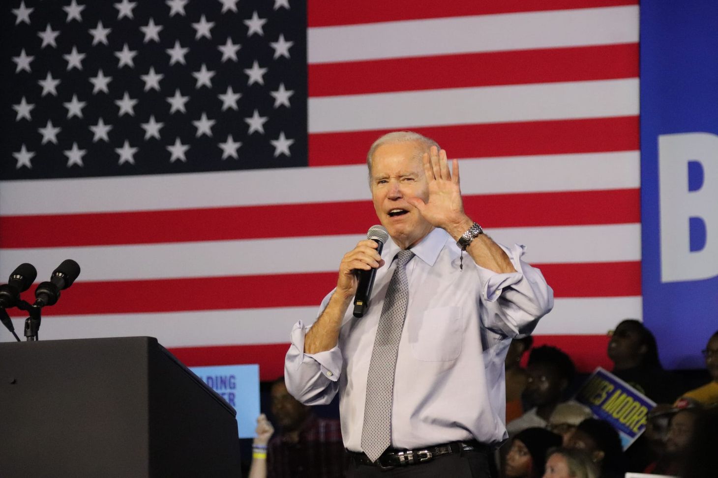 Biden speaking adjacent to a podium and in front of a large American flag at a rally.